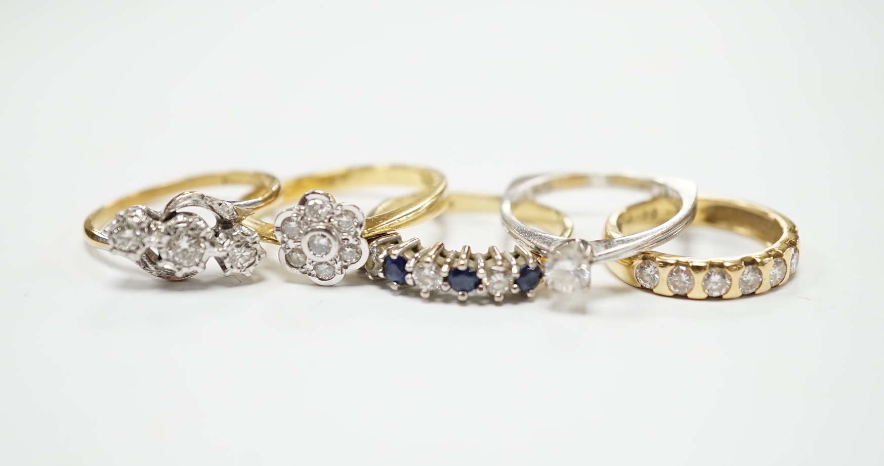 Four assorted 18ct and diamond set rings, including solitaire, flower head cluster, three stone crossover and seven stone half hoop, together with and 18ct sapphire and diamond set half hoop ring, gross weight 15.6 grams